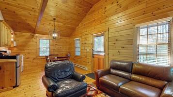 A log cabin interior with a dining area, leather seating, and a kitchen.