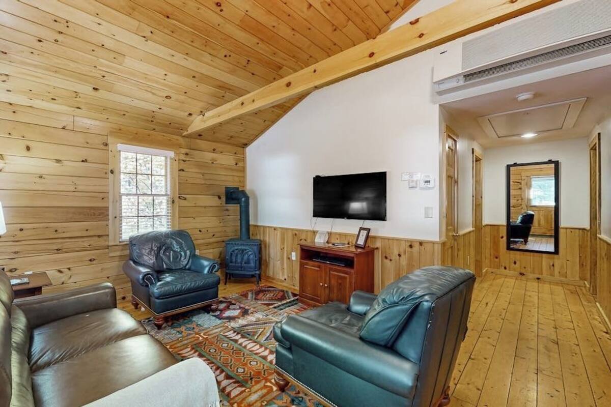 Interior de una cabaña de troncos con chimenea, sofás de cuero, televisor y un espejo.