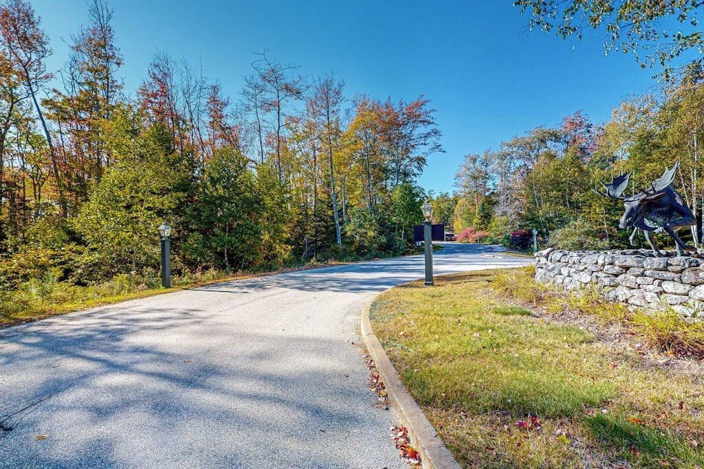 A paved road curving through a wooded area with autumn foliage, a stone wall, and a statue of moose.