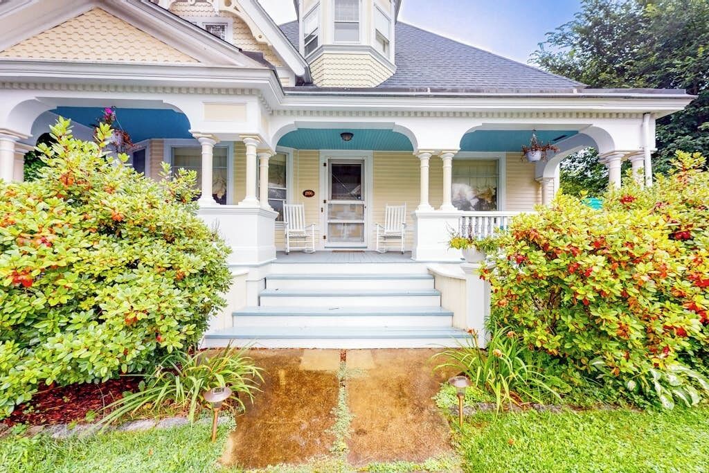 Uma casa de dois andares com varanda, degraus que levam à entrada e um jardim bem cuidado.
