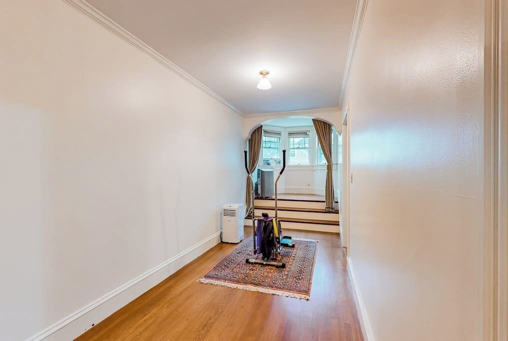 A narrow hallway with a wooden floor, a standing heater, and a rug.