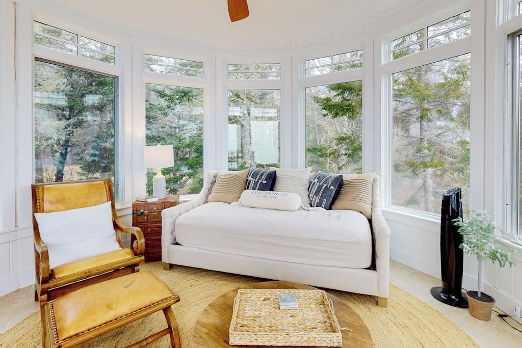 A bedroom with a large window, a bed, a chair, a bedside table, and a floor lamp.