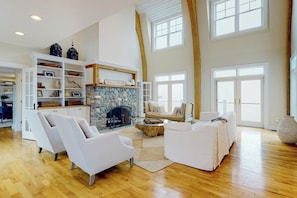 A spacious living room with a stone fireplace, white sofas, and a high ceiling with large windows. - Spectacular Oceanfront Retreat With Amazing Views, Sunroom & Washer/dryer (Georgetown)