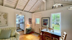 A cozy room with a wooden ceiling, a dining table with chairs, a kitchen area, and a large window with a view. - Whispering Spruces; Cozy Studio With Queen Bed & W (South Thomaston)