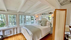 A bedroom with a large bed, a window with a view of trees, a lamp, and a wooden ceiling. - Whispering Spruces; Cozy Studio With Queen Bed & W (South Thomaston)
