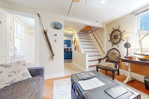 Ein Wohnzimmer mit einer Couch, einem Couchtisch, einem Sessel, einem Steuerrad und einer Treppe zu einem anderen Raum.