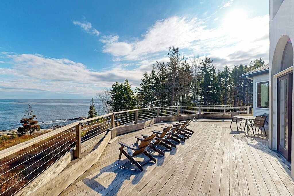 A wooden deck with chairs and tables, overlooking the ocean and trees.