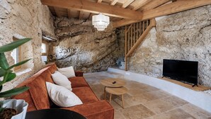 A rustic interior with a stone wall, wooden ceiling beams, a sofa, a TV, and a small round table. - Maison Cøva: The Essentials in Their Raw Form (Castelnau-sur-l'Auvignon)