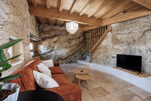 Ein rustikales Interieur mit einer Steinwand, Holzbalkendecke, einer Couch, einem Fernseher und einem kleinen runden Tisch.