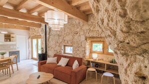 A rustic interior with a stone wall, wooden beams, a sofa, a dining table, and a kitchen area. - Maison Cøva: The Essentials in Their Raw Form (Castelnau-sur-l'Auvignon)