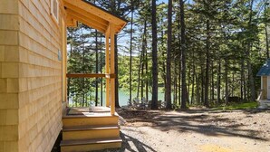 Eine Holzhütte mit Veranda, einem Kiesweg und einem bewaldeten Gebiet mit einem See im Hintergrund.