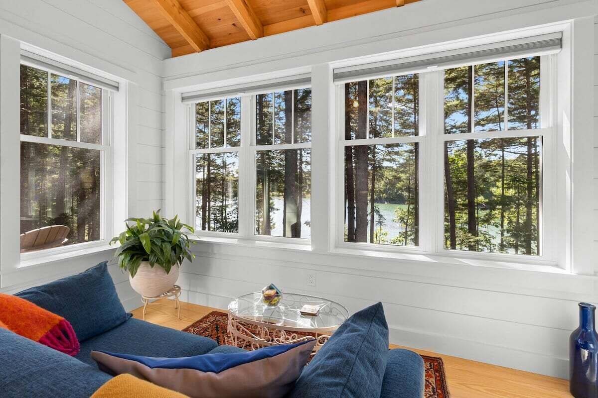 A room with a wooden ceiling, white walls, and large windows with a forest view.