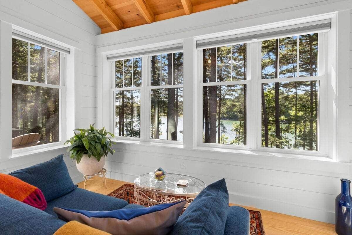 A room with a wooden ceiling, white walls, and large windows with a forest view.