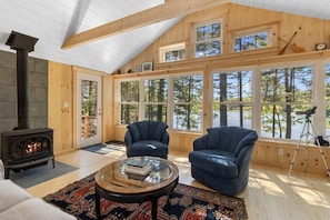 Interior acogedor de una cabaña con chimenea, ventanas amplias y techo de madera rústica.