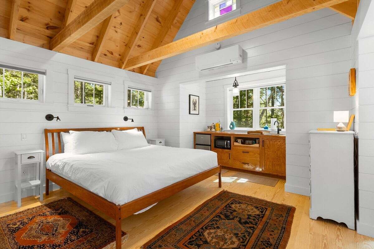A bedroom with a wooden bed, white walls, a wooden ceiling, and a window.