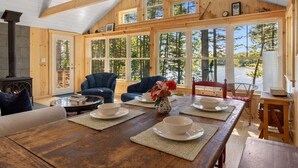 Ein gemütliches Blockhaushaus-Interieur mit einem Holzespeisesaal, gedeckt für vier Personen, einem Kamin und großen Fenstern mit Blick auf den Wald.