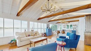 A spacious living area with a large window, a wooden ceiling, and a blue sofa. - Charming Cottage: Deepwater Dock, Panoramic Linekin Bay Views, Near Village (Boothbay)