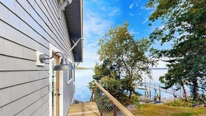A wooden deck leading to a house with a view of a lake and dock. - Charming Cottage: Deepwater Dock, Panoramic Linekin Bay Views, Near Village (Boothbay)