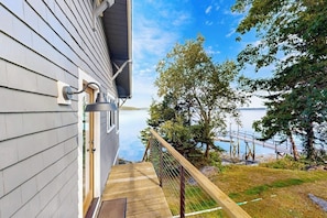 A wooden deck leading to a house with a view of a lake and dock. - Charming Cottage: Deepwater Dock, Panoramic Linekin Bay Views, Near Village (Boothbay)