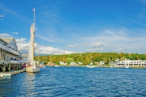 A waterfront scene with a sailboat docked at a pier, buildings along the shore, and a clear sky. - Amazing All-season Sprucewold Cabin w/ Private Beach Club Access Dog-friendly (Boothbay Harbor)
