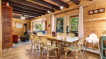 A wooden interior with a dining table surrounded by wicker chairs, a sofa, and a red chair.