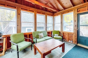 A cozy cabin interior with a wooden ceiling, large windows, a green sofa, a wooden table, and a door. - Waterfront Cabin w/ Outdoor Firepit, Dock, and Lake Views - Dogs Welcome (Greenville)