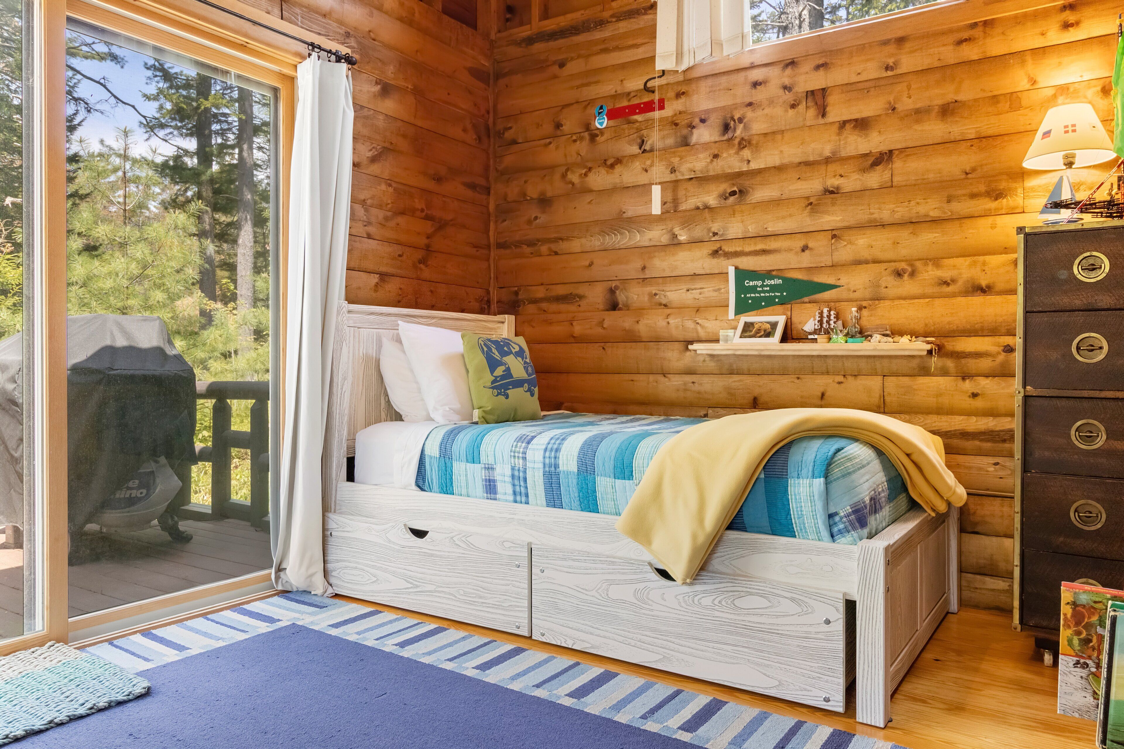 Un dormitorio de cabaña de madera con cama, cómoda, ventana y un cartel en la pared.