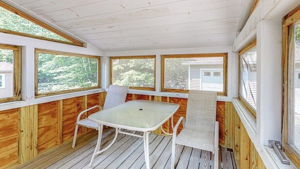 A covered porch with a table and two chairs, wooden walls, and large windows. - Inviting Dog-friendly Home With Firepit & Ping-pong - Near Acadia National Park (Ellsworth)