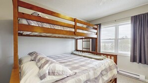 Een slaapkamer met stapelbed, raam, gordijnen en plafondventilator.