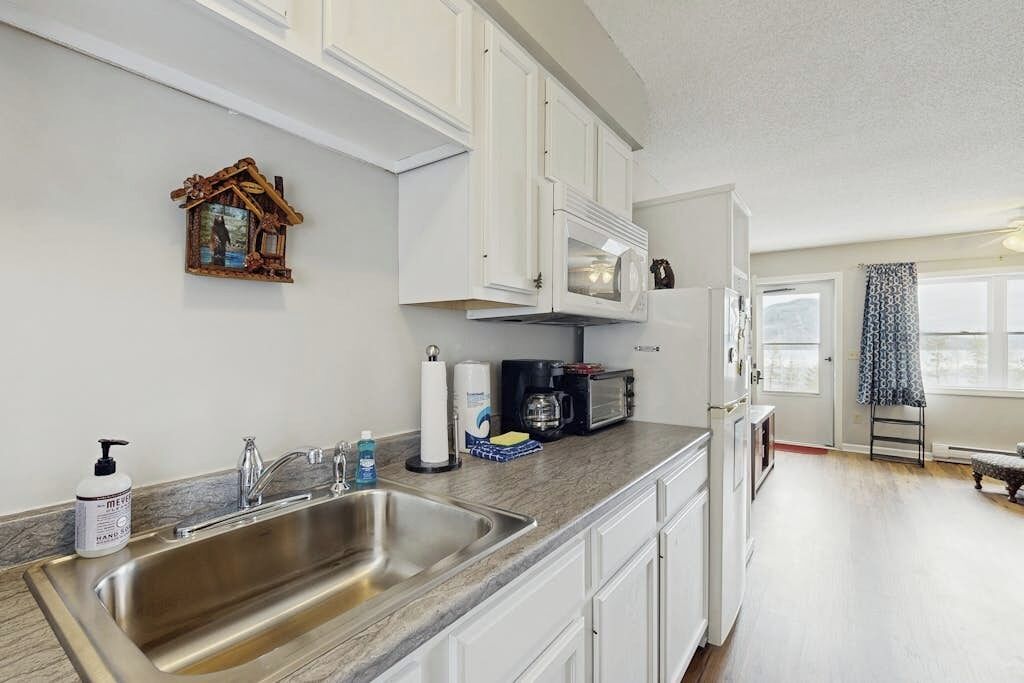A kitchen with white cabinets, a stainless steel sink, a microwave, and a coffee maker.