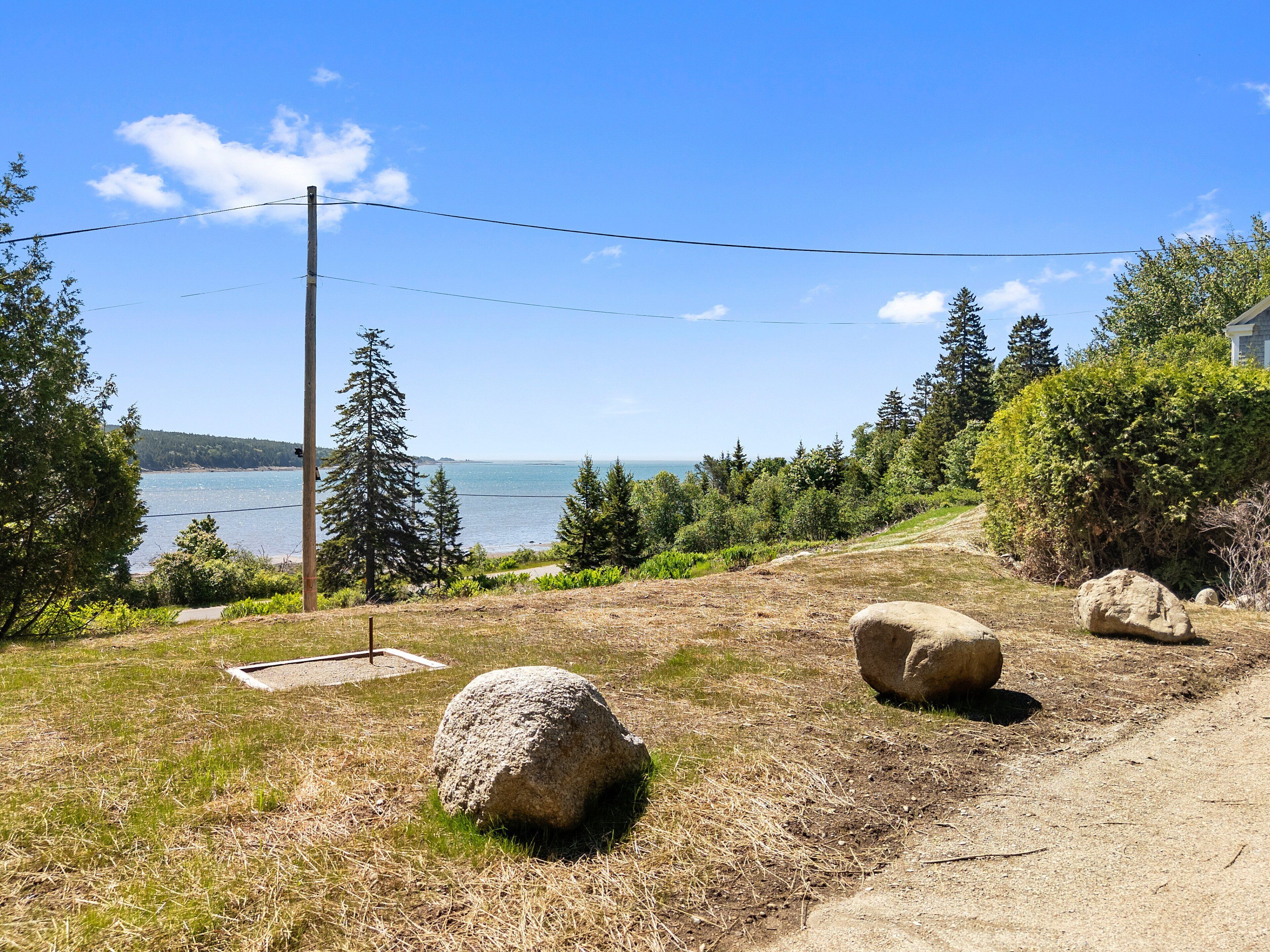 Eine Küstenlandschaft mit einem Feldweg, großen Felsen und Blick auf das Meer.