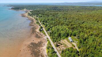 An aerial view of a coastal area with a road running alongside a beach, surrounded by dense forest.