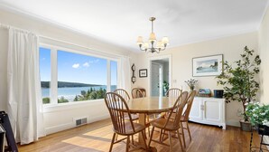 A dining area with a wooden table and chairs, a chandelier, and a view of the sea. - Dog-friendly Oceanfront Home With Private Shorefront, two Fireplaces, & Firepit (Steuben)