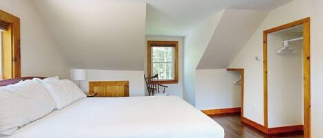 A bedroom with a bed, a window, a chair, and a wooden floor.