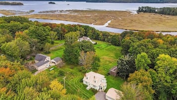 A large house surrounded by dense trees and a body of water.