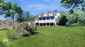 A two-story house with a covered porch, surrounded by a well-maintained lawn and trees. - Dog-friendly, Bay View Home With Wifi & Laundry - Close to Baxter State Forest (Bowdoinham)