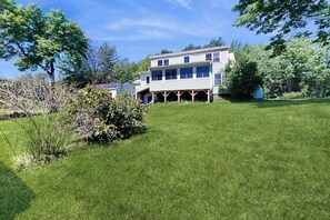 A two-story house with a covered porch, surrounded by a well-maintained lawn and trees. - Dog-friendly, Bay View Home With Wifi & Laundry - Close to Baxter State Forest (Bowdoinham)