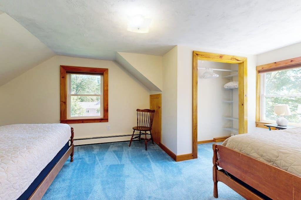 Un dormitorio con dos camas, una silla, una puerta de madera y una ventana.