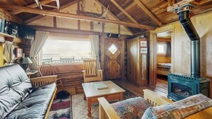 A cozy cabin interior with a fireplace, wooden furniture, and a window overlooking a scenic view. - Dog-friendly Lakefront Cabin With Private Dock, Epic Views of Lake & Mt Kineo (Rockwood)
