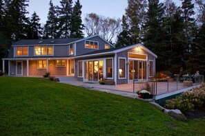 Ein zweistöckiges Haus mit überdachter Terrasse und gepflegtem Rasen.