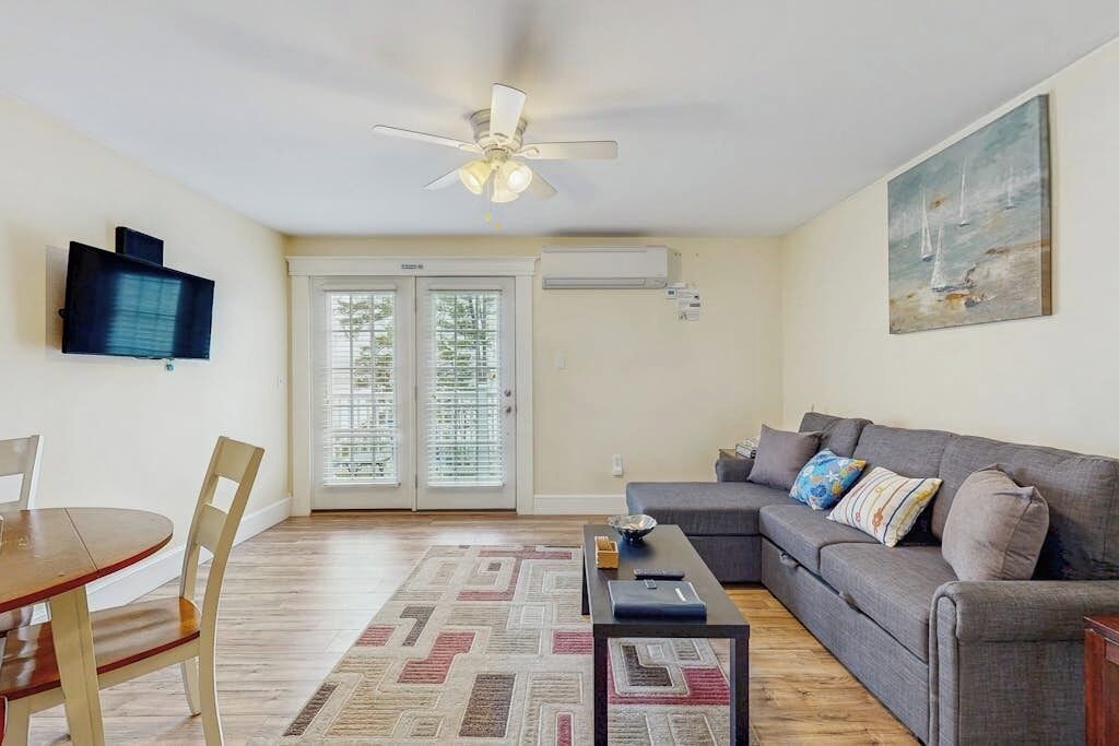 A living room with a sofa, a coffee table, a TV mounted on the wall, and a ceiling fan.