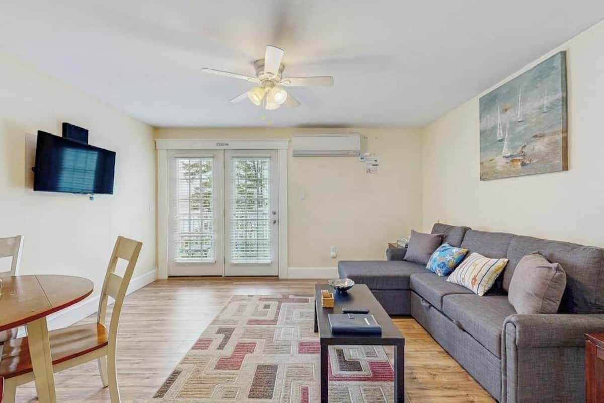 A living room with a sofa, a coffee table, a TV mounted on the wall, and a ceiling fan.