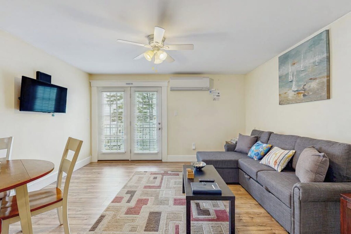 A living room with a sofa, a coffee table, a TV mounted on the wall, and a ceiling fan.