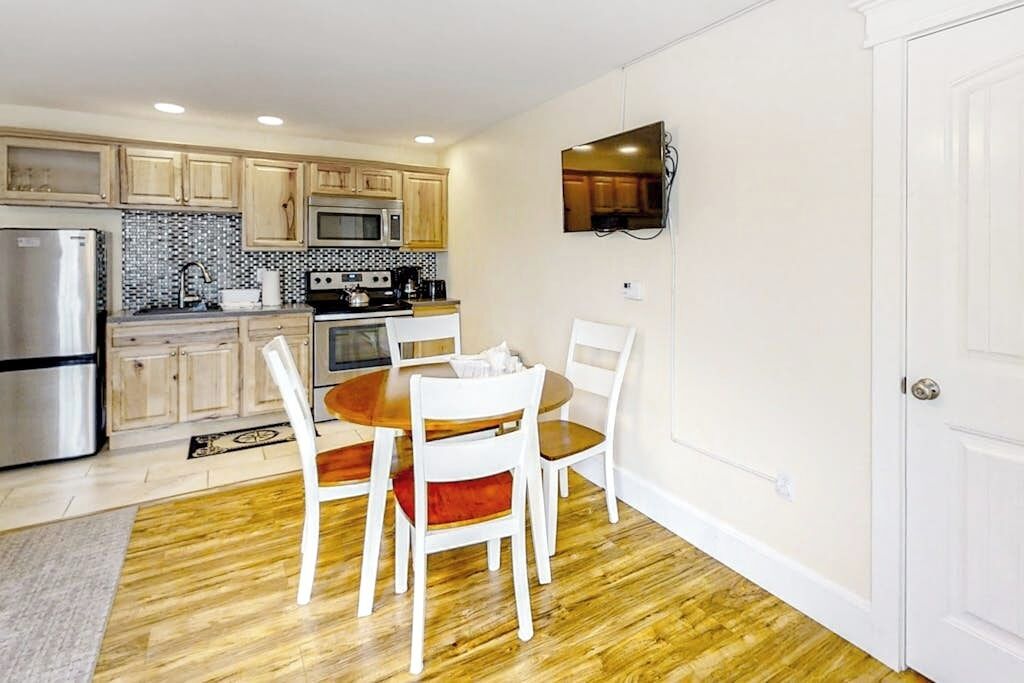 A compact kitchen with wooden cabinets, a microwave, a refrigerator, and a dining table with chairs.