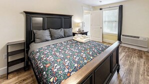 Un dormitorio con cama, mesitas de noche, una ventana con persianas y una puerta.