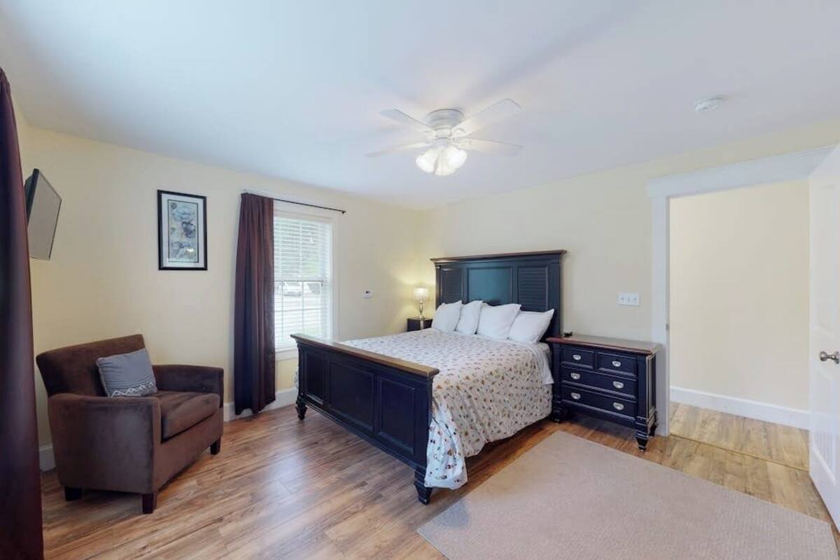 A bedroom with a bed, a dresser, a chair, a ceiling fan, and a window with curtains.