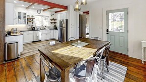 Una cucina con mobili bianchi, elettrodomestici in acciaio inossidabile, un tavolo da pranzo in legno e un lampadario.