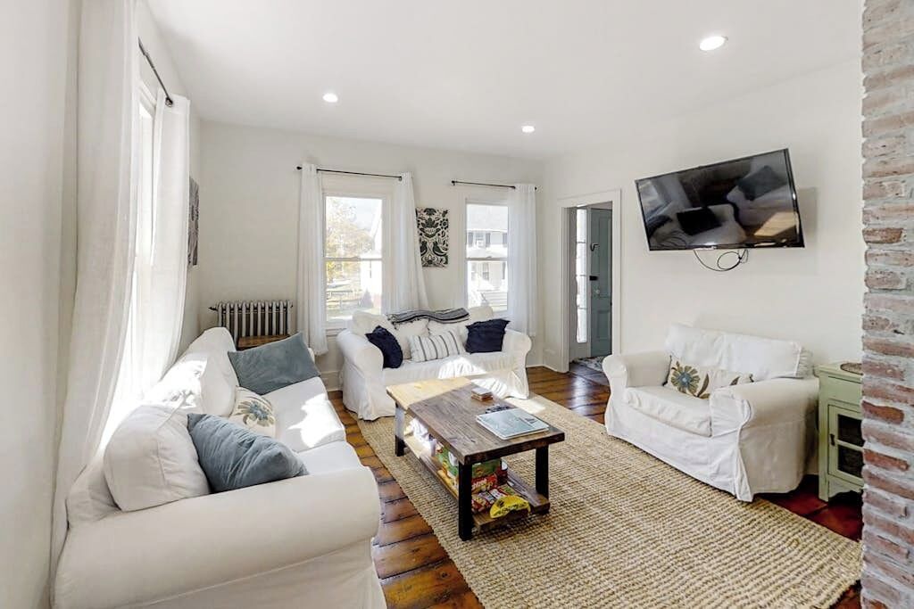 A modern living room with white sofas, a coffee table, and a TV mounted on the wall.