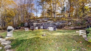 Ambiente naturale all'aperto con prato, mobili da giardino bianchi e terreno roccioso.