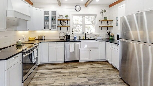 Una cucina moderna con mobili bianchi, un frigorifero in acciaio inossidabile e pavimento in legno.